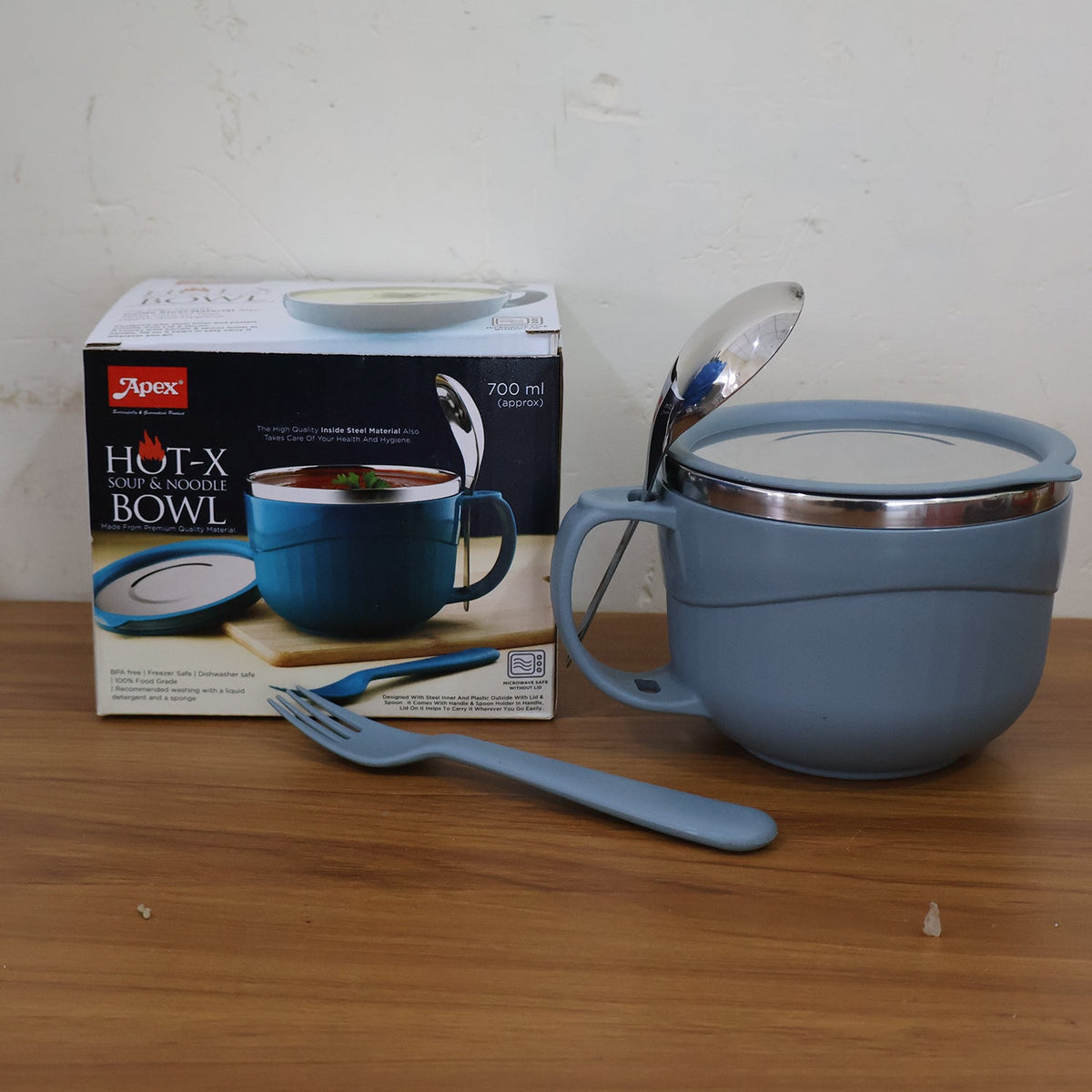 A blue insulated bowl with a lid, spoon, and fork next to its product box on a wooden surface.