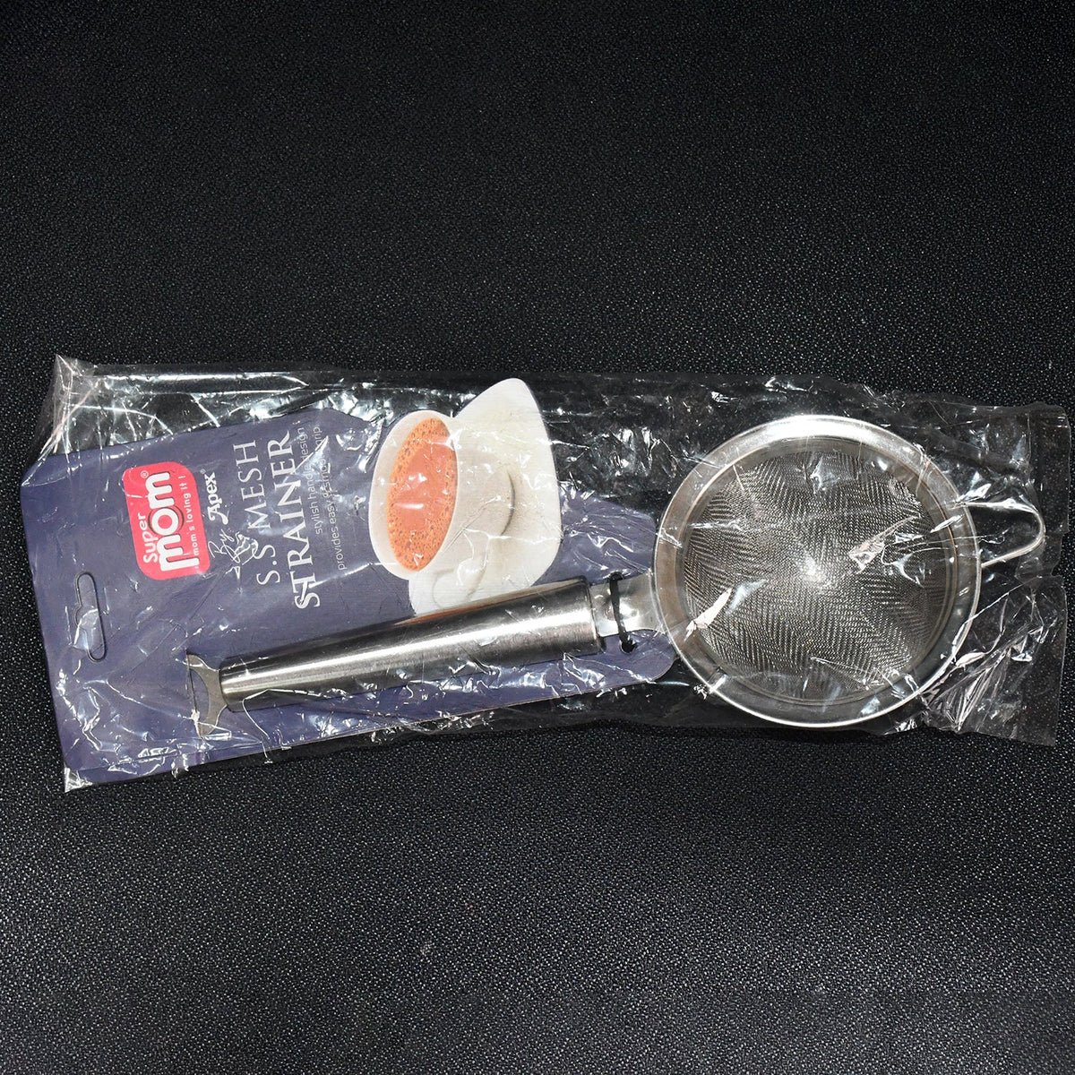 A stainless steel fine mesh strainer is packaged in clear plastic with a branded label, lying flat on a dark background.