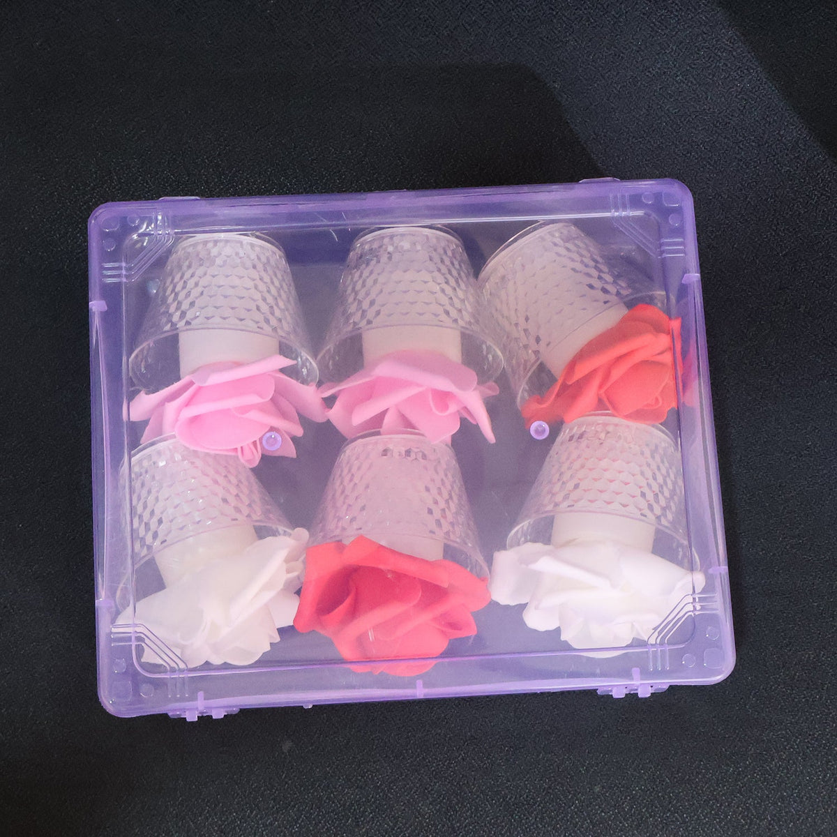 Six rose-shaped LED candles, pink, red, and white, packaged in a clear purple plastic box on a dark surface.