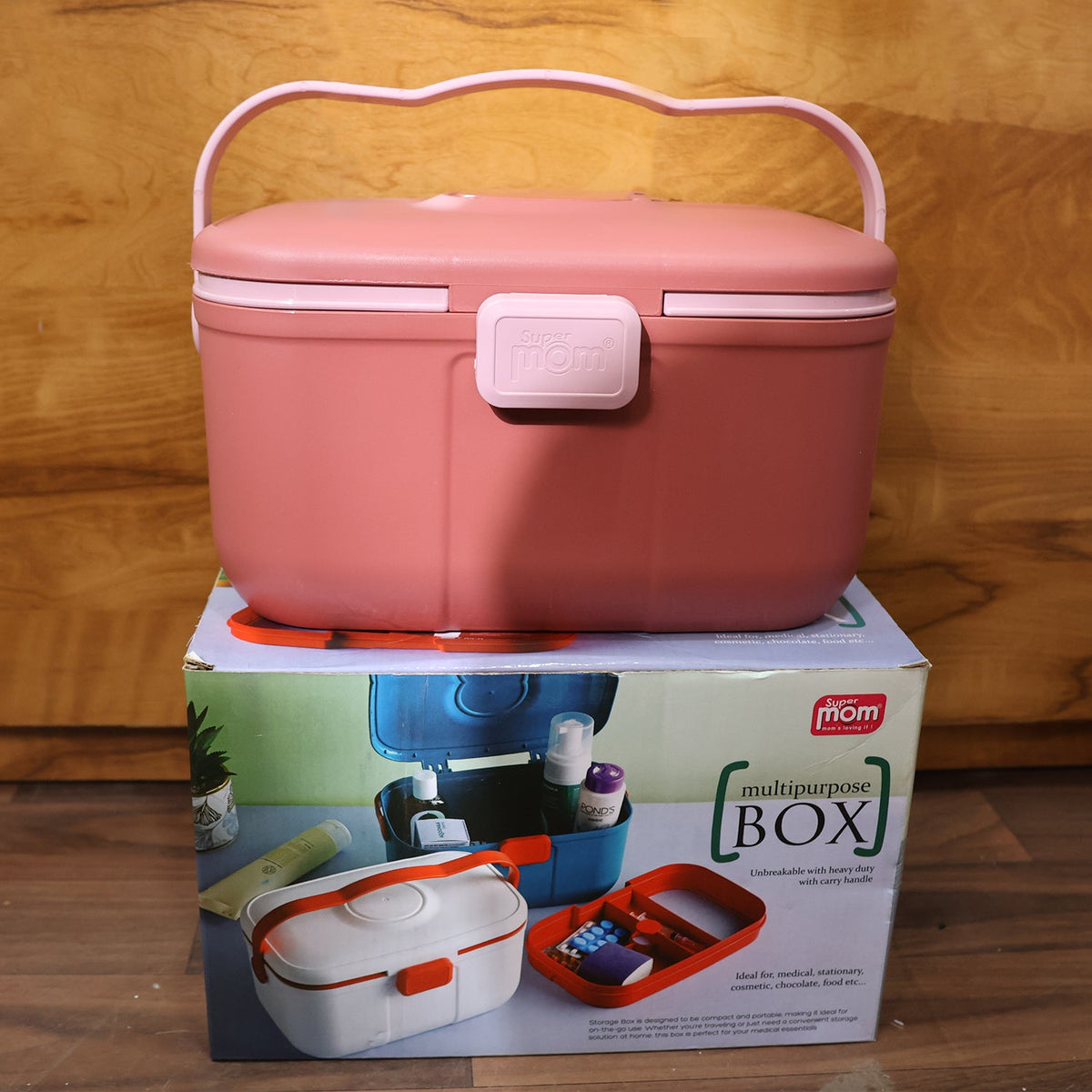 Closed pink storage box with a wavy handle sitting on top of its product packaging box, against a wooden background.