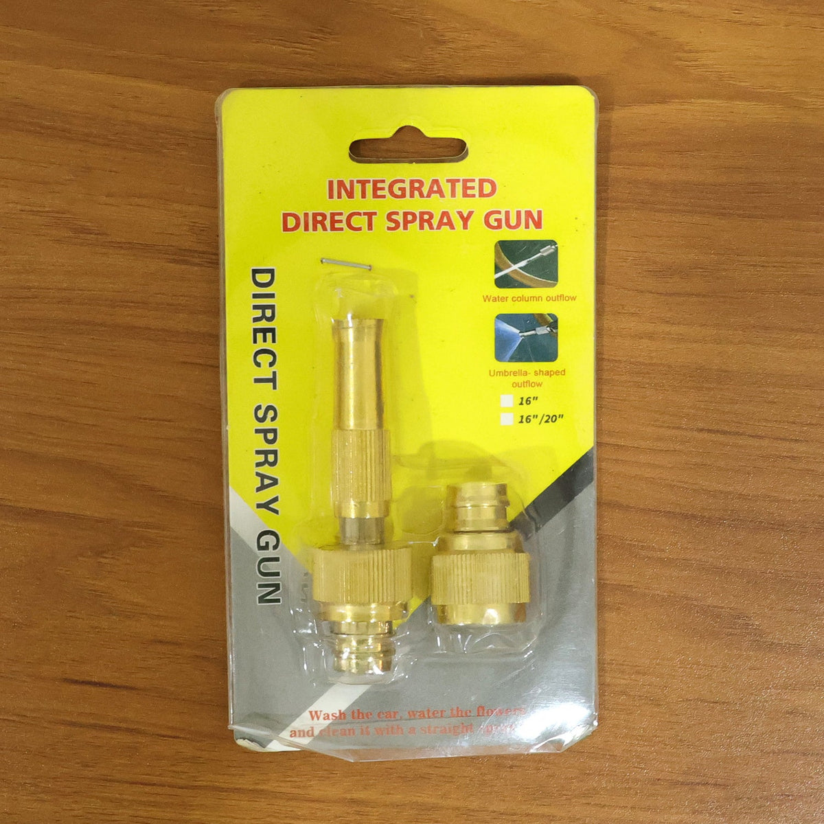 A brass spray gun and connector are packaged in clear plastic on a yellow card, displayed on a wooden surface.