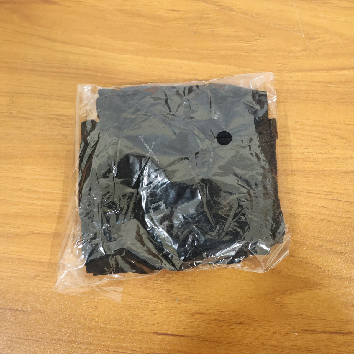 A single pair of black compression sleeves neatly folded inside a clear plastic package on a wooden surface.