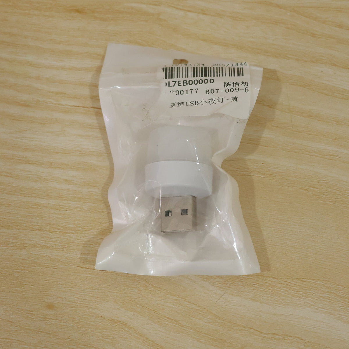 A white USB mini light bulb sealed in a clear plastic bag with a label, resting on a light wooden surface.