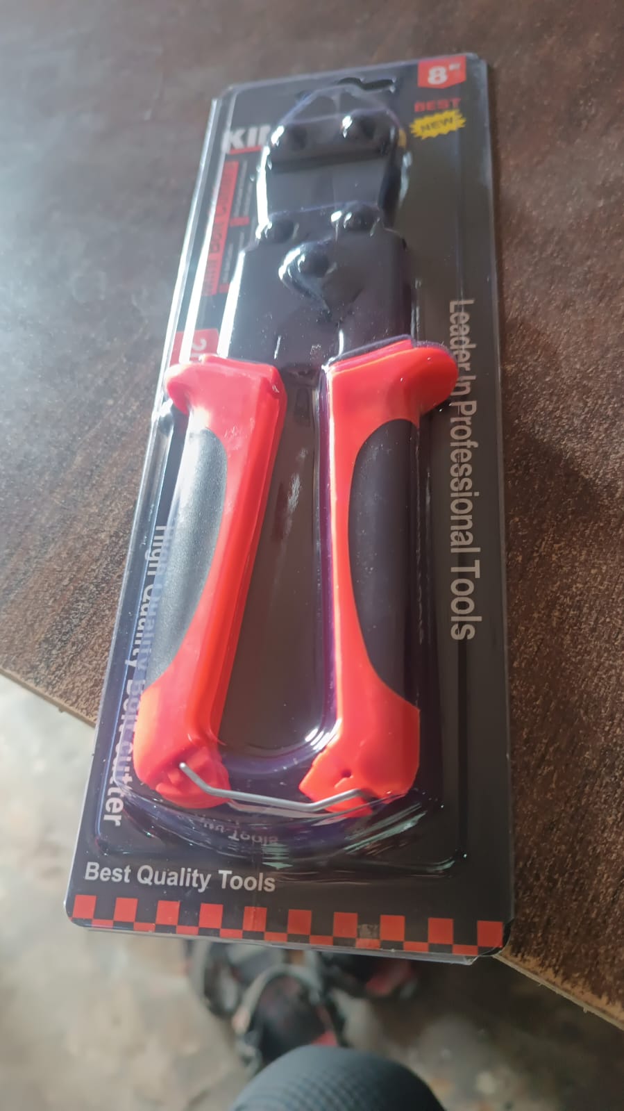Mini bolt cutters with red and black handles, sealed in clear retail packaging on a wooden surface.