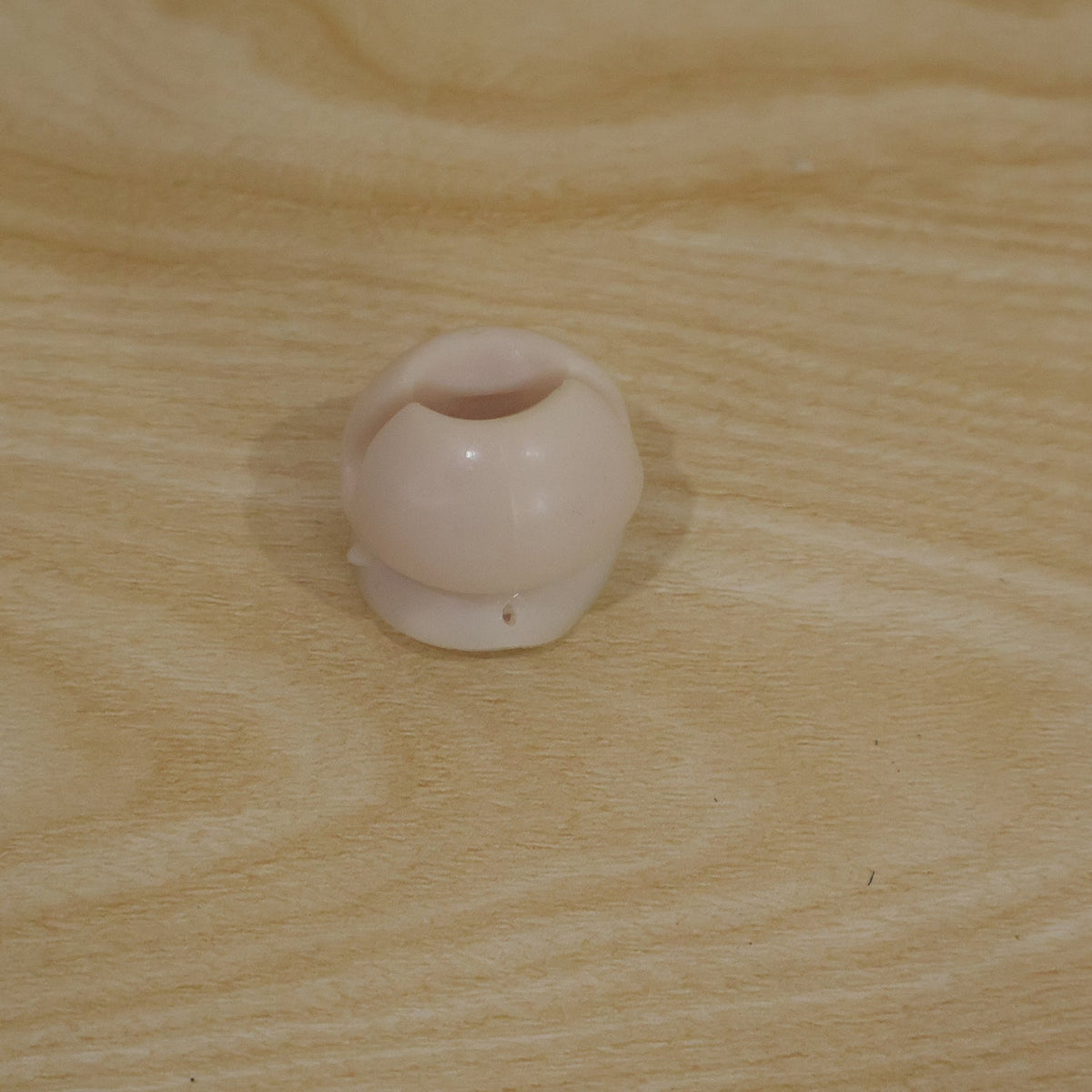 A single white toothbrush holder clip resting on a light brown wooden surface.