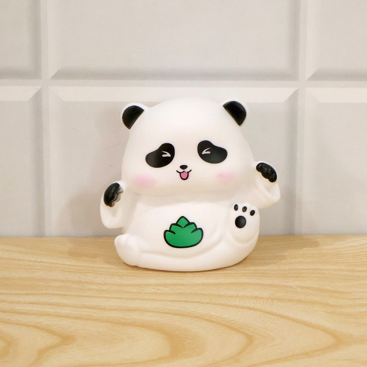 A white panda night light with black details and a green leaf, sitting on a light wooden surface.
