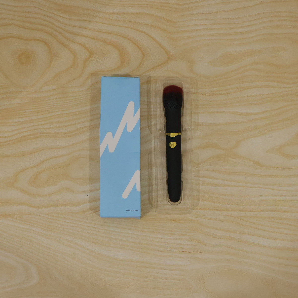 A black and red makeup brush with gold accents is used by a woman to apply blush to her cheek, with a USB port detail.