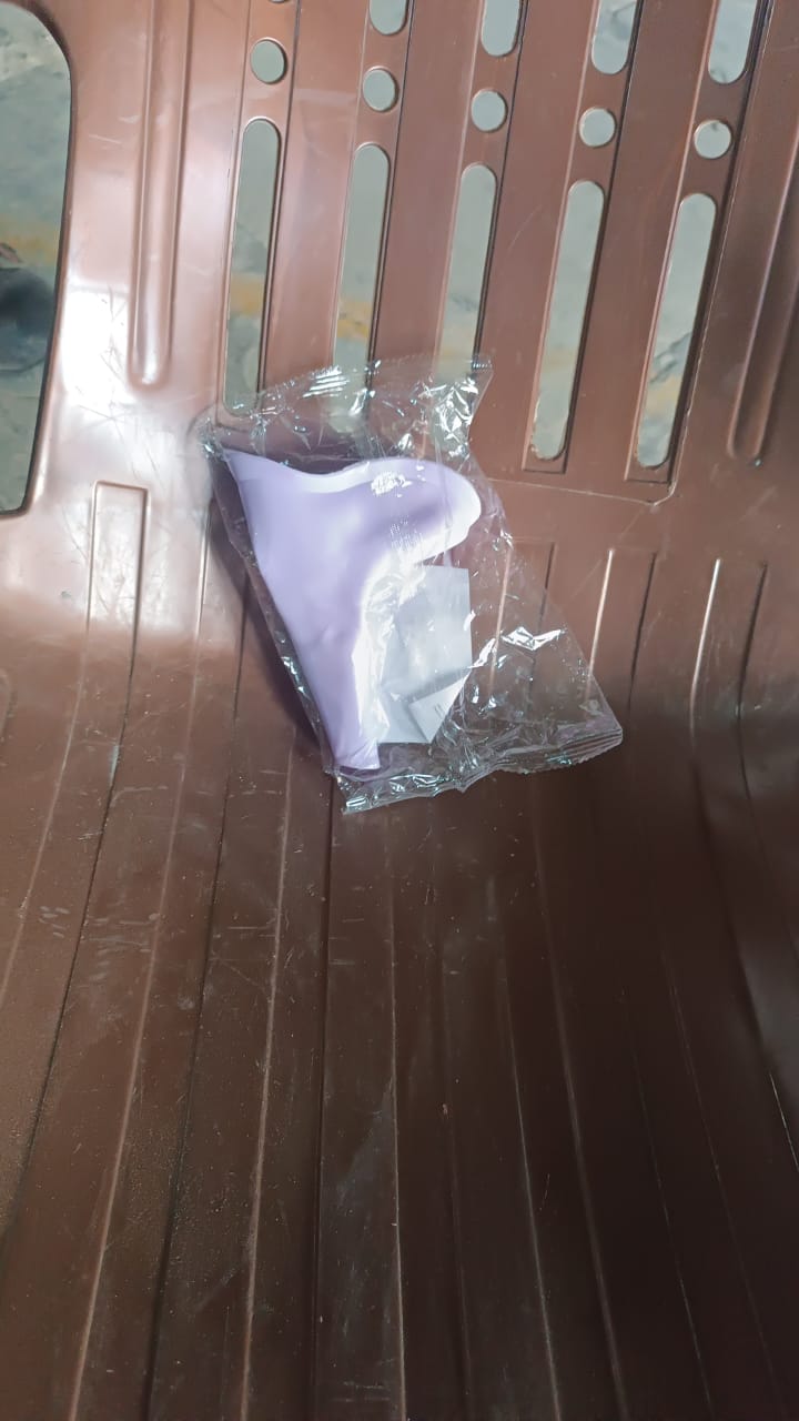 A purple silicone urination funnel is partially visible inside clear plastic packaging, resting on a brown chair.