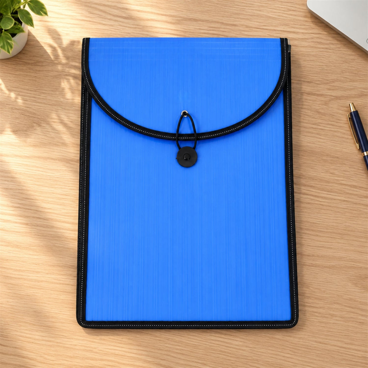 A blue plastic document folder with a black elastic closure, lying flat on a wooden desk with a laptop and plant nearby.