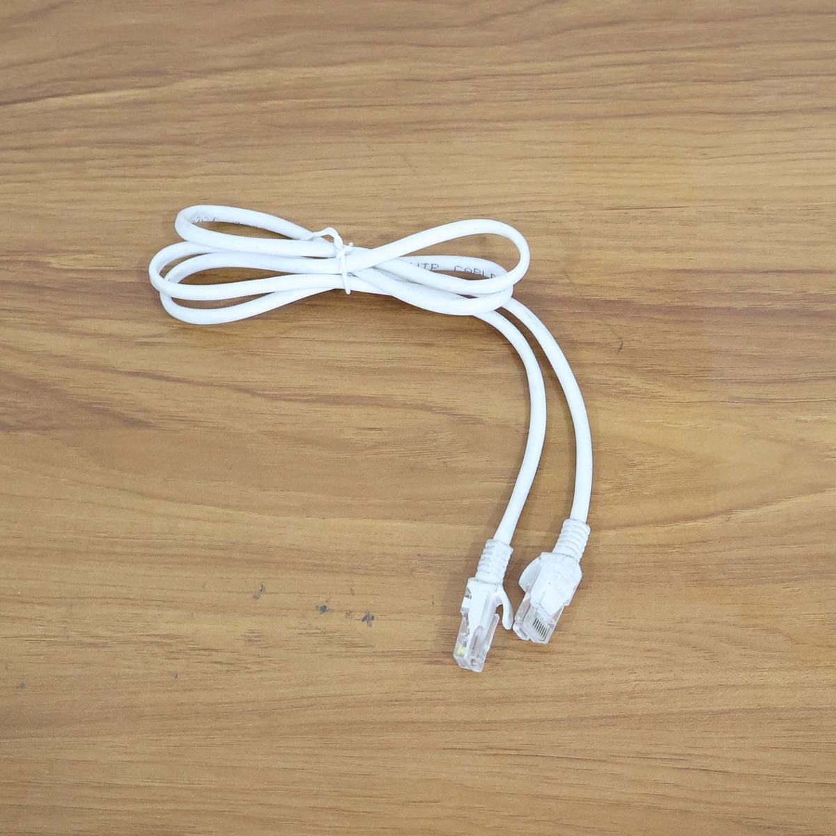 A coiled white ethernet cable with two clear plastic connectors is displayed on a wooden surface.