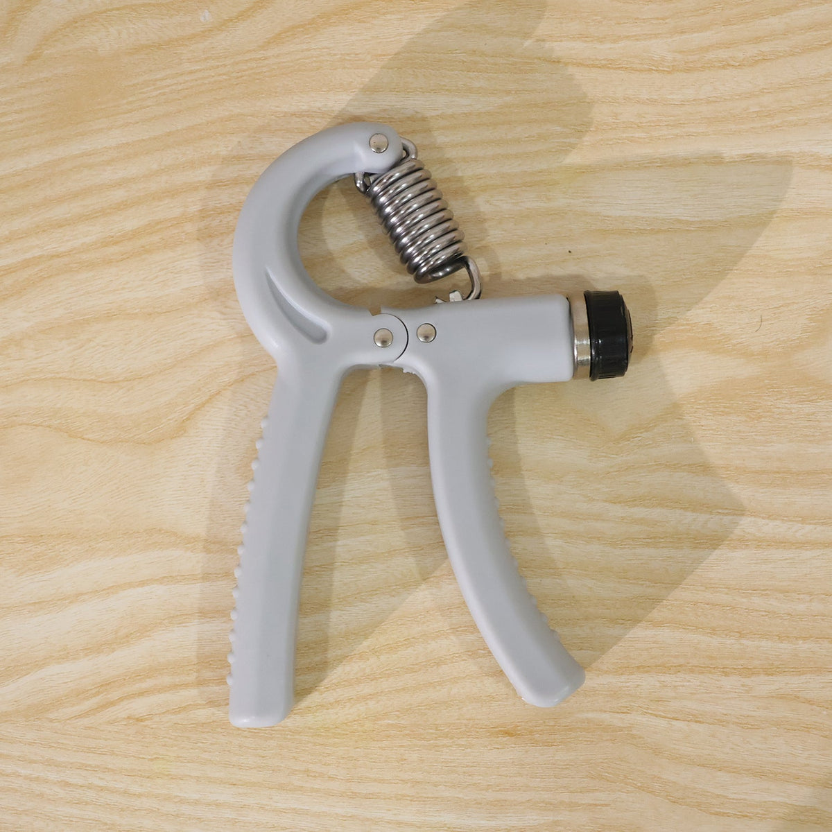 A gray adjustable grip strength trainer with a metal spring rests on a light wooden surface.