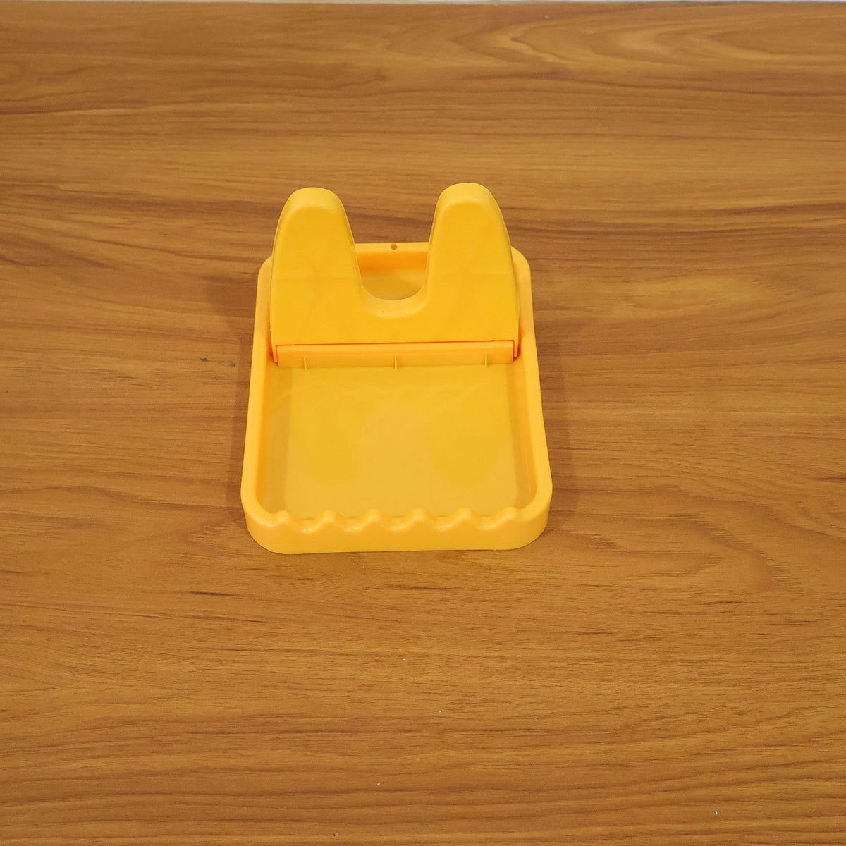An empty yellow plastic lid and spoon rest centered on a light brown wooden table.