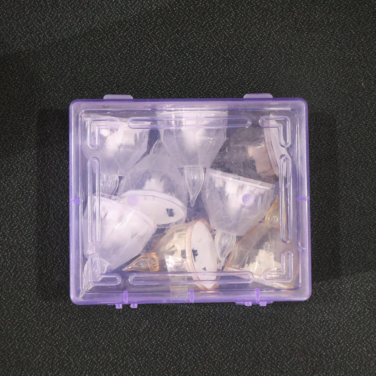 A clear plastic box filled with several clear and amber crystal-style LED diyas on a dark gray surface.