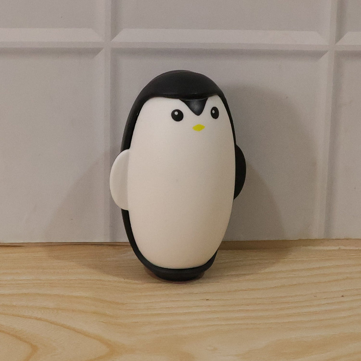 A black and white penguin lint roller stands upright on a light wooden surface against a white tiled wall.