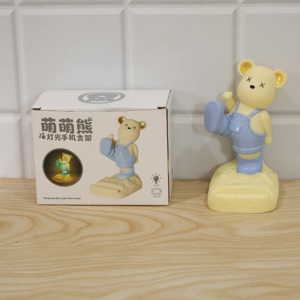 A yellow bear phone holder with blue overalls next to its product box on a wooden surface.