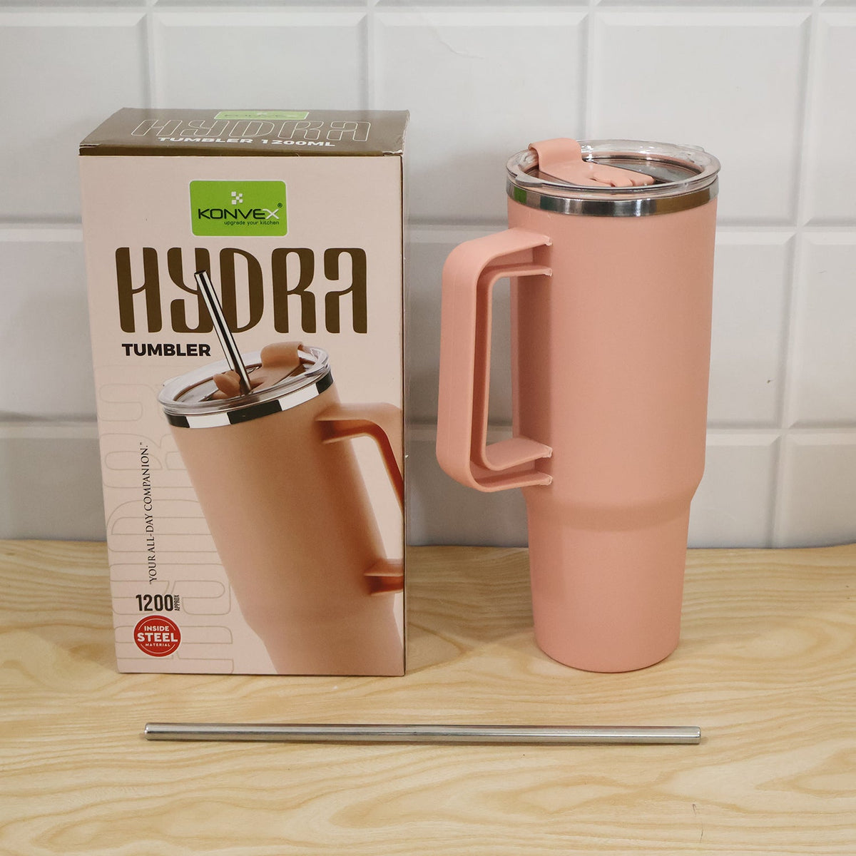 A pink tumbler with its packaging box and a metal straw are displayed on a wooden surface.
