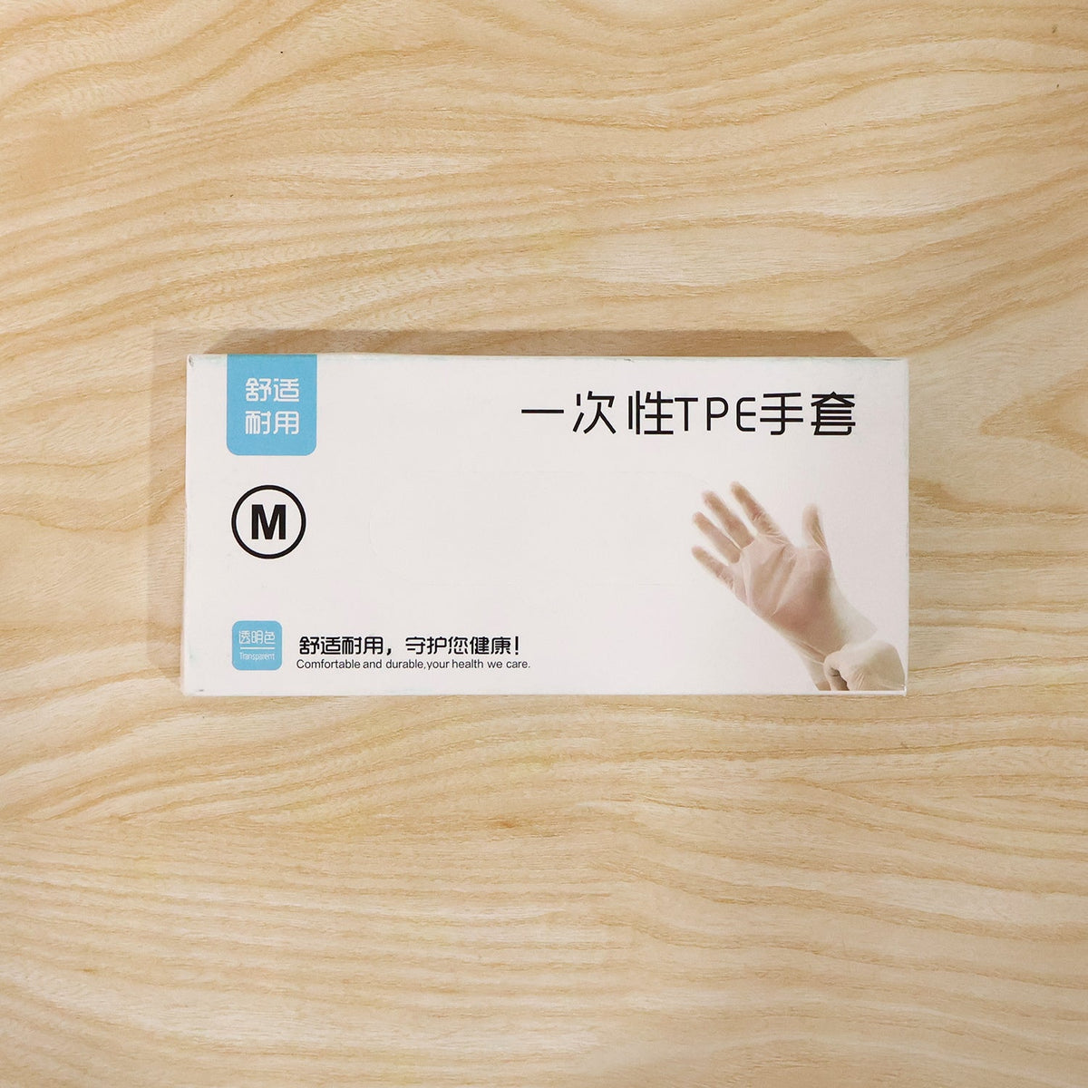 A white dispenser box for disposable gloves, labeled with Chinese characters and an 'M', on a wooden surface.