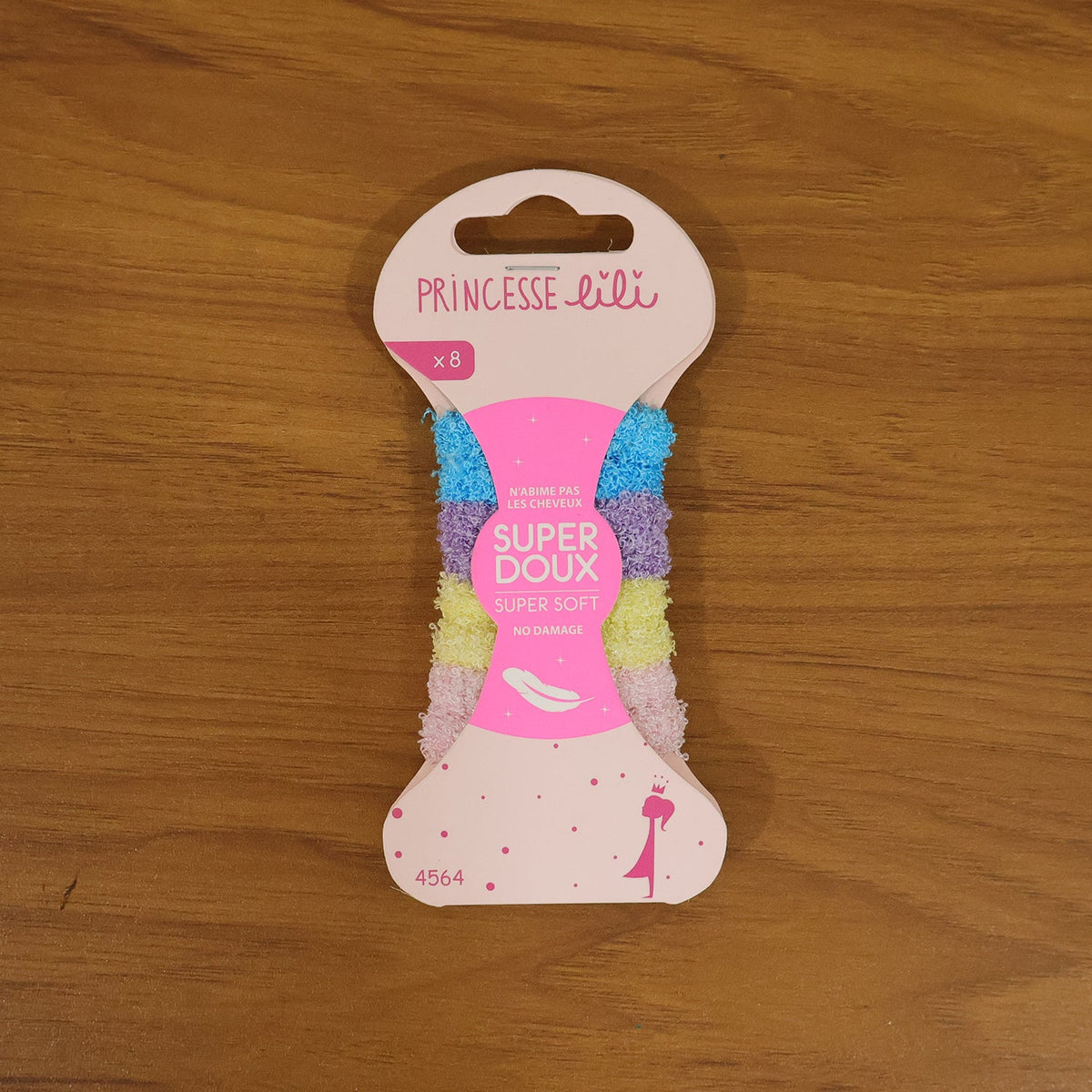A pink package of 'Princesse Lili' hair bands, labeled 'Super Doux' and 'Super Soft', sits on a wooden surface.