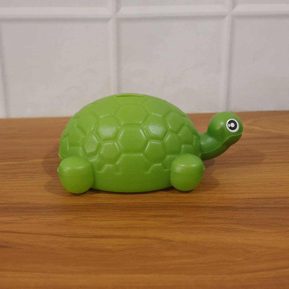 A green plastic turtle money bank with a textured shell sits on a polished wooden surface.