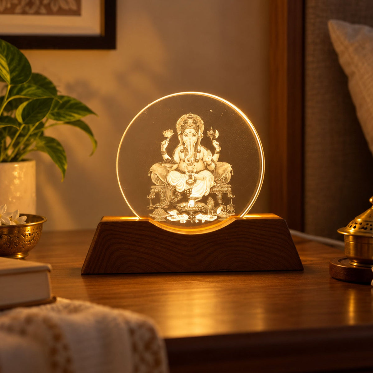 Illuminated Ganesha LED lamp on a wooden base, glowing warmly on a dark brown bedside table with a green plant.