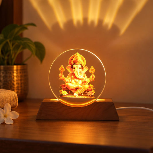 A Ganesha acrylic lamp with a warm glow sits on a wooden base on a table, projecting light onto the wall.