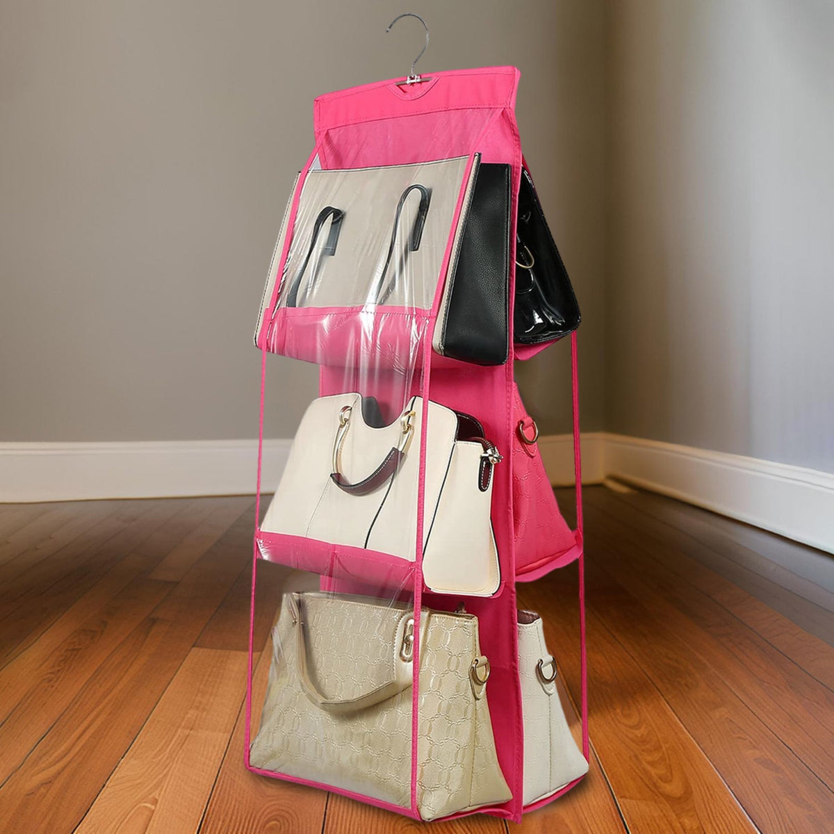 A pink hanging purse organizer with clear pockets, filled with handbags, stands on a wooden floor.
