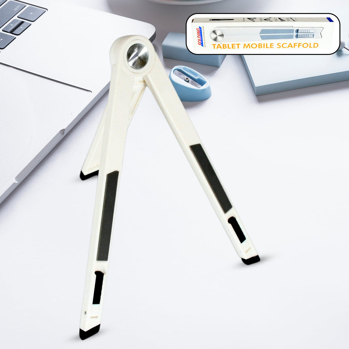 A white foldable stand with black grip pads is open on a white desk next to a laptop and pencil sharpener.