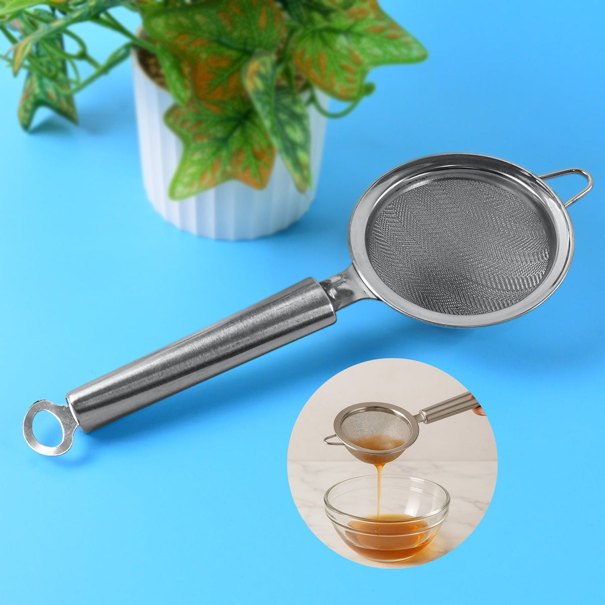 A stainless steel fine mesh strainer with a long handle is centered on a blue background, with a small plant behind it and