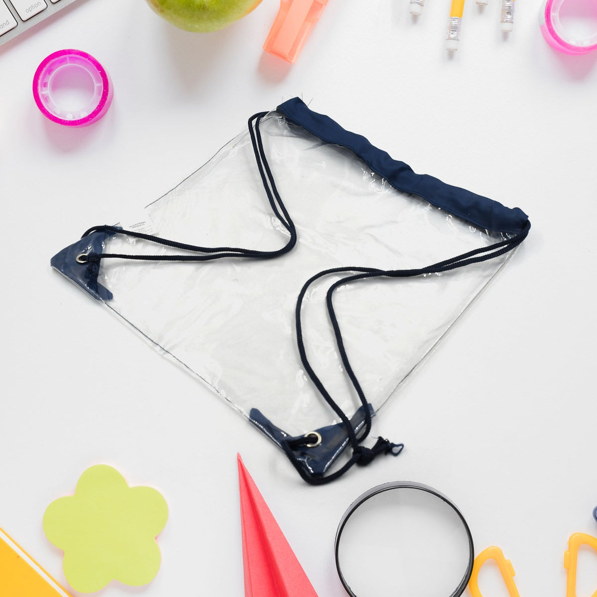 Clear drawstring bag with dark blue cords and accents, lying on a white desk surrounded by school supplies.