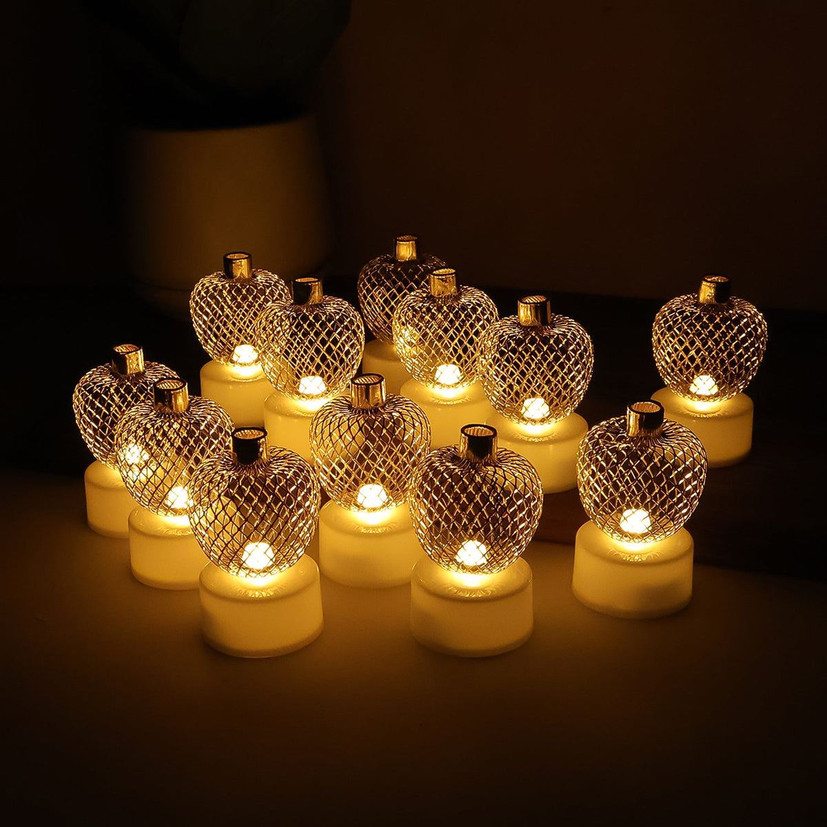 Twelve glowing gold mesh LED tealights arranged in four rows of three, creating a warm ambiance in a dimly lit setting.