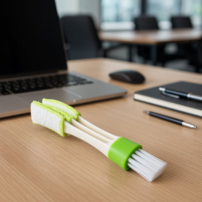 A white and green 3-in-1 cleaning brush resting on a wooden desk with a laptop and office supplies.