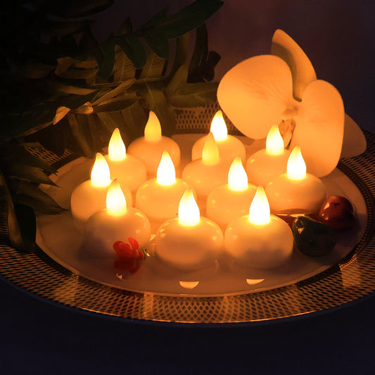 Twelve white LED floating candles with warm yellow flames on a decorative plate with a white orchid and green leaves.