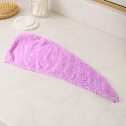 A purple microfiber hair drying wrap towel is laid flat on a white marble countertop next to a brush and cotton swabs.