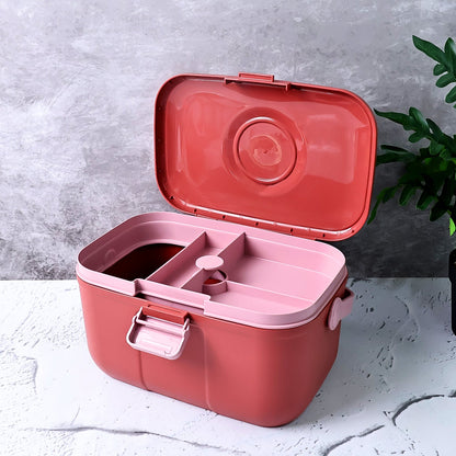 Open red and pink plastic storage box with internal compartments on a grey surface next to a plant.
