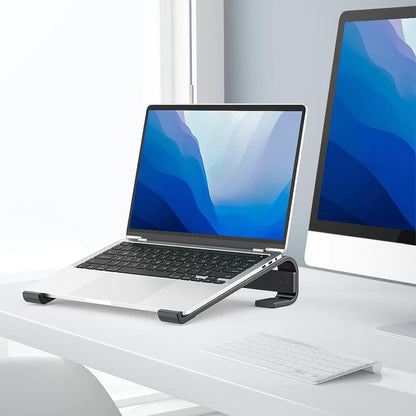 A silver laptop sits on a black metal stand on a white desk next to a monitor.