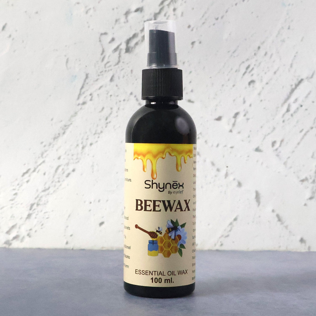 A black 100ml spray bottle of Shynex Beeswax essential oil wax with a white textured background.