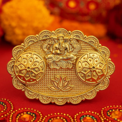 A close-up of a gold-finished chopra featuring an embossed Ganesh, two ornate round containers, and a lotus design on a red