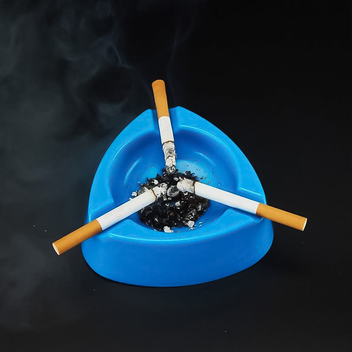 Three lit cigarettes rest in a blue plastic ashtray filled with ashes, emitting smoke against a dark background.