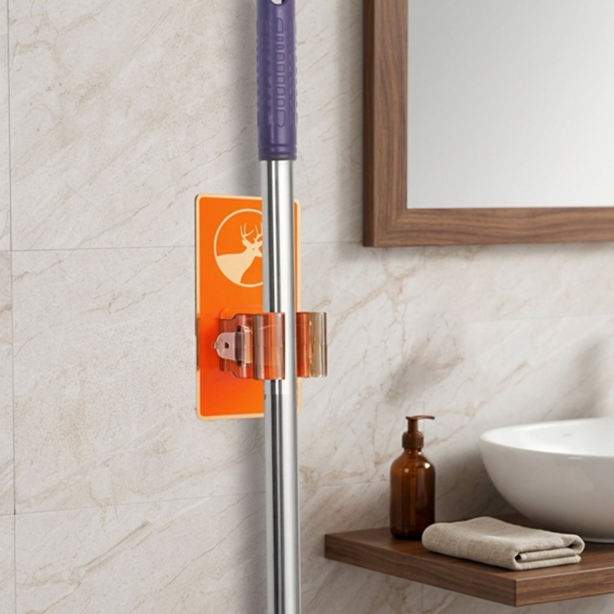 An orange deer-themed wall-mounted holder on a light tiled wall, holding a mop, with a sink and mirror in the background.