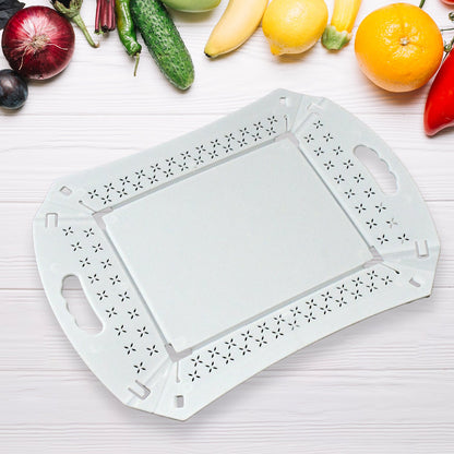 A white foldable serving tray lies flat on a white wooden surface surrounded by fresh fruits and vegetables.
