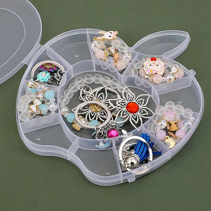 A close-up of an open transparent apple-shaped organizer box, revealing various colorful beads, charms, and rings in its