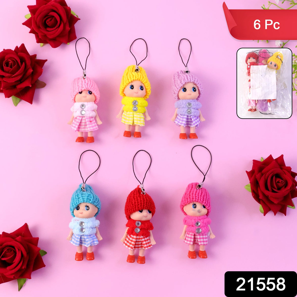Six colorful doll keychains with knitted hats are arranged on a pink surface with red roses.