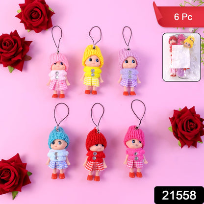 Six colorful doll keychains with knitted hats are arranged on a pink surface with red roses.