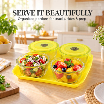 Four glass bowls with yellow lids on a tray, two filled with salad and fruit in a kitchen setting.