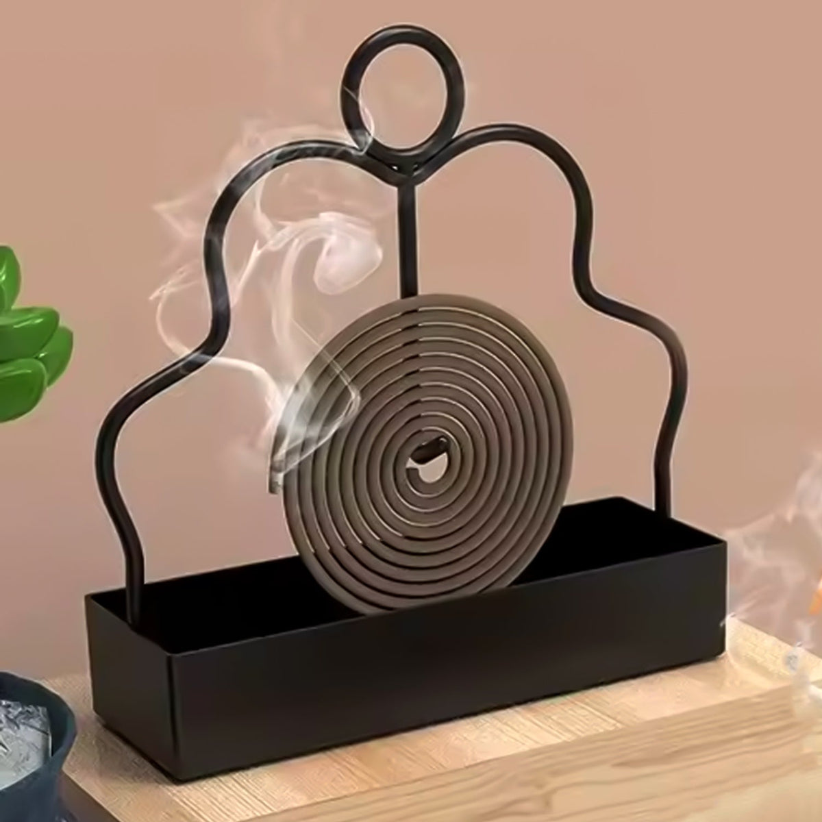 A black metal mosquito coil holder with a burning brown spiral coil emitting smoke on a wooden surface.