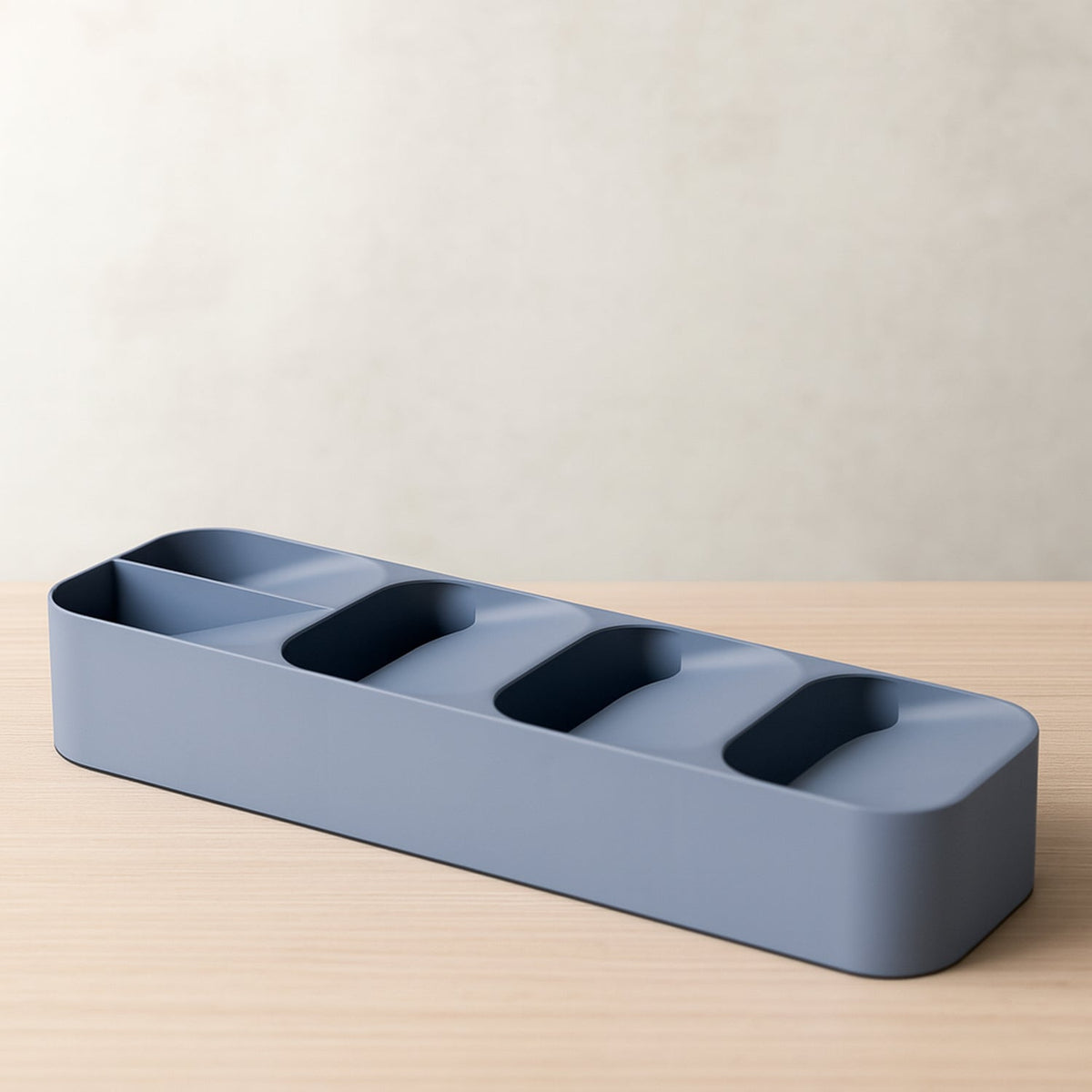 A gray plastic cutlery organizer with five compartments rests on a light wooden table against a neutral wall.