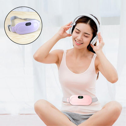 A woman wearing headphones and a pink heating pad on her lower abdomen, sitting cross-legged and smiling.