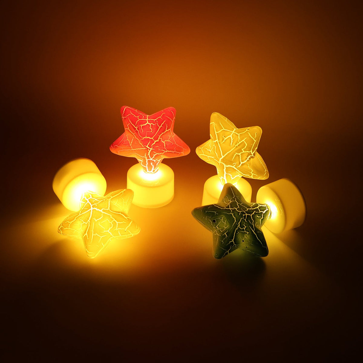 Four glowing star-shaped LED tealight candles in red, green, and two yellow, with two bases detached.