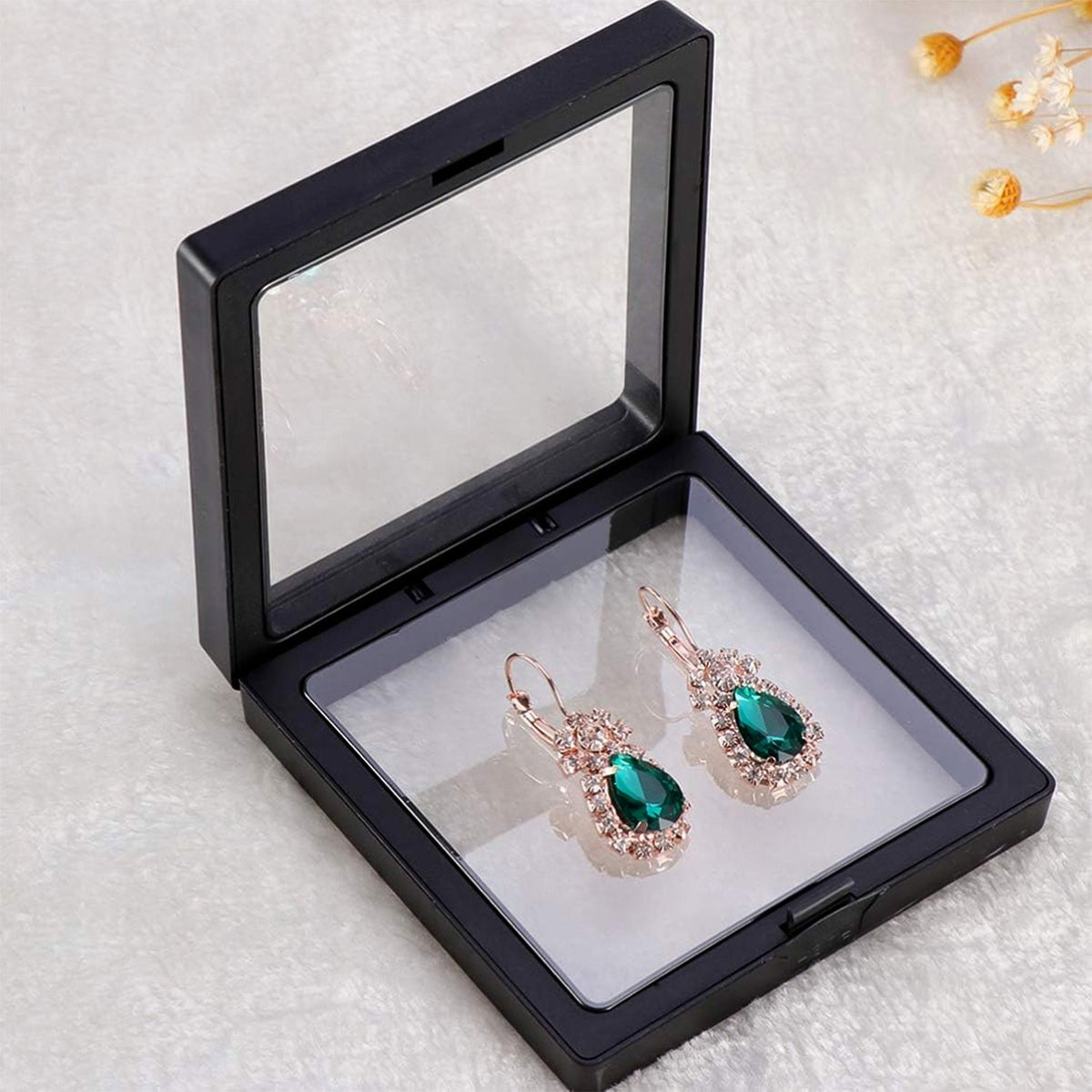 Open black square display box with clear film, showcasing a pair of emerald and rose gold earrings.