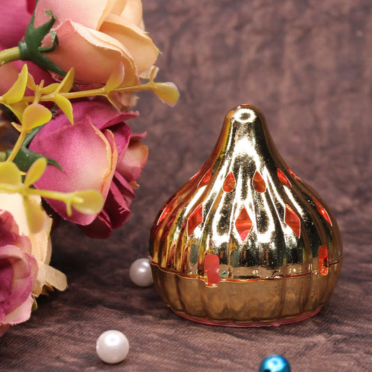 A gold modak-shaped LED light with red diamond cutouts sits next to pink flowers and white pearls.